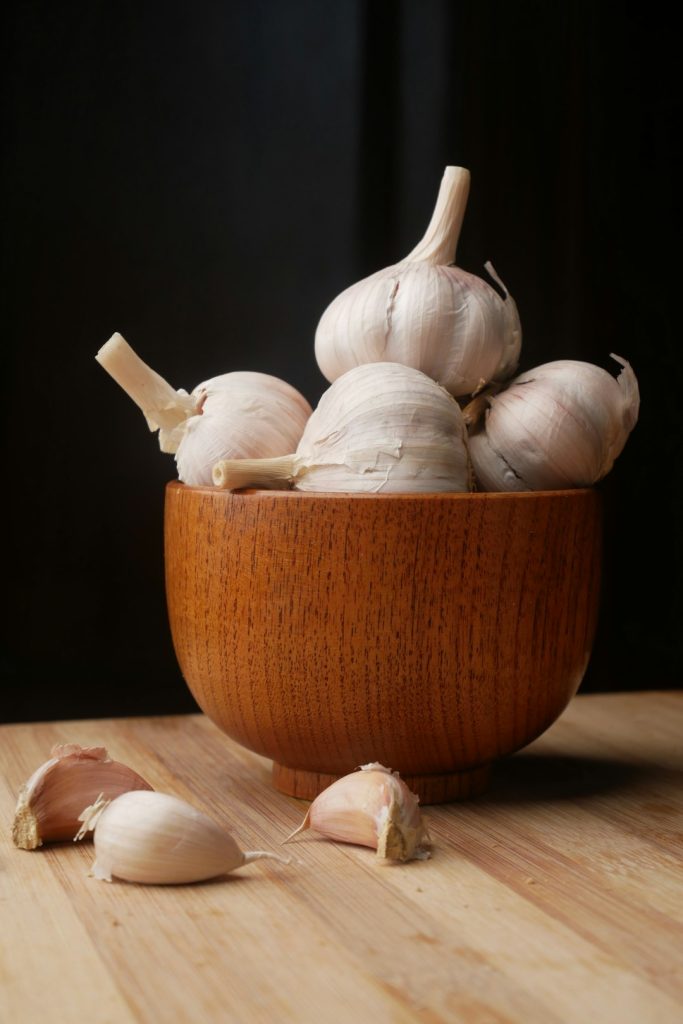 Fresh garlic bulbs in a wooden bowl with a few cloves on a wooden surface, suitable for natural remedies and home health tips.