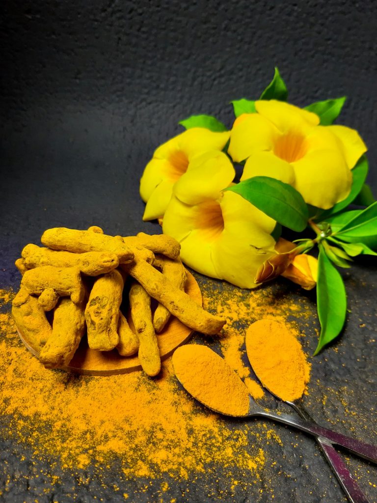Fresh turmeric roots and turmeric powder with yellow flowers and green leaves on a dark background, highlighting natural remedies for health and wellness.