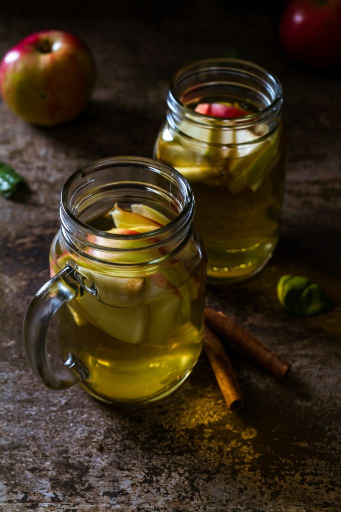 Refreshing apple cider vinegar detox drinks with sliced apples and cinnamon sticks over rustic wooden table for natural health remedies.